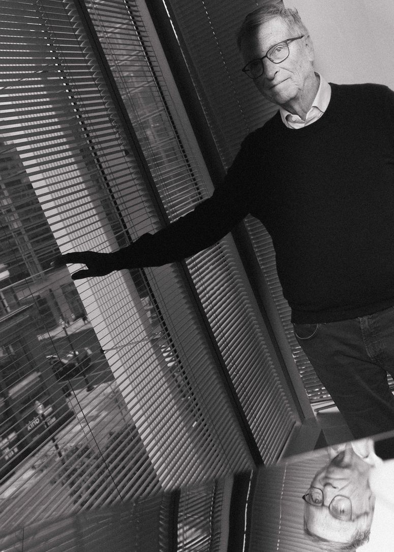 Bill Gates alcanzando las persianas de la ventana con su reflejo en un espejo debajo