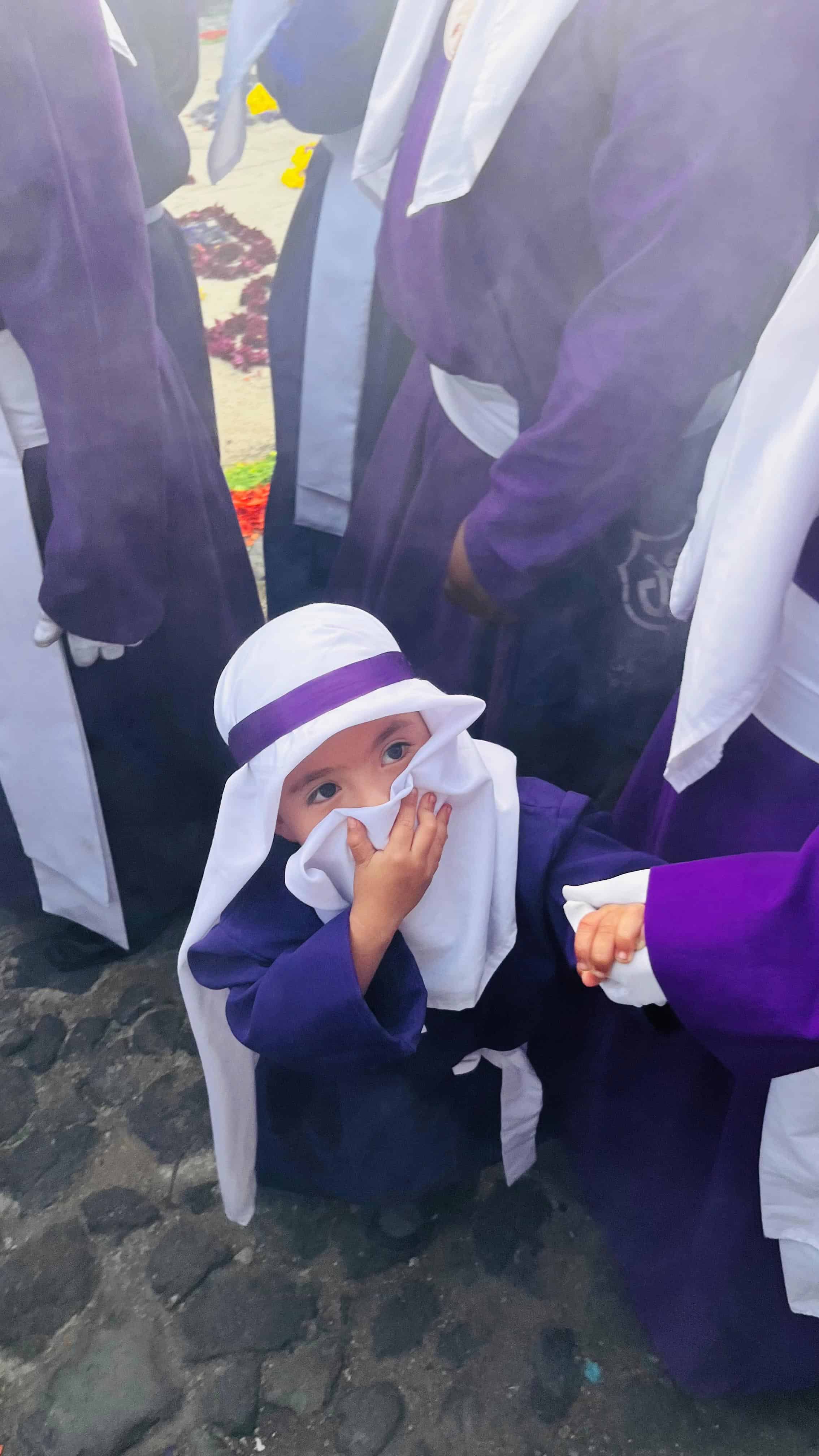 Un niño vestido de cucurucho se protege del fuerte olor del incienso.
