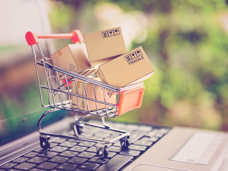 Carrito de compra en miniatura con pequeñas cajas de cartón en su interior, sobre las teclas de una laptop